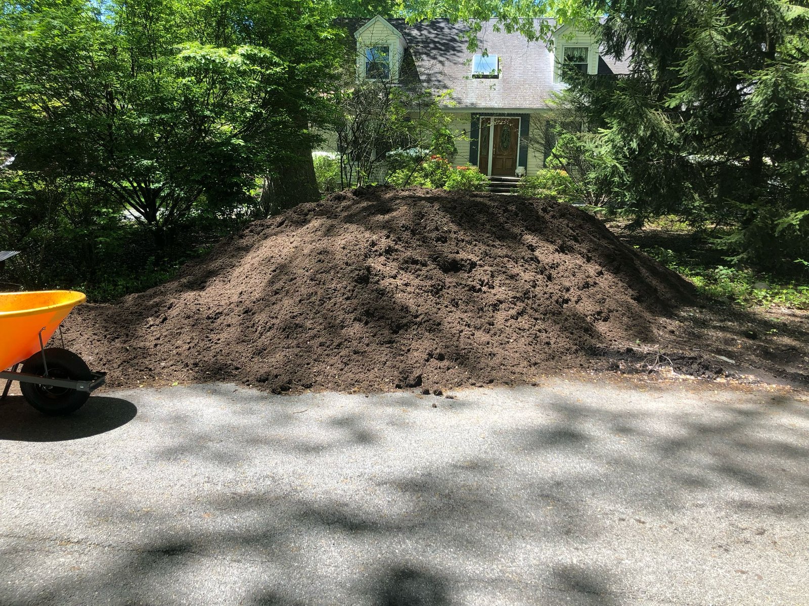 Twelve-yard pile of screened topsoil beside driveway awaiting landscape installation.